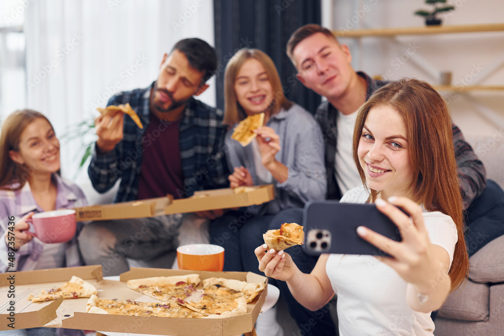 Woman making selfie. Group of friends have party indoors together