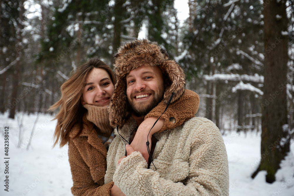 People, season, love and leisure concept - happy couple hugging and laughing outdoors in winter. Couple embracing and having fun in snowy winter park