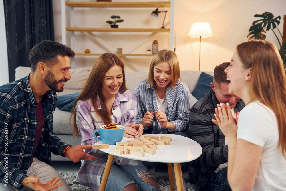 Wooden tower has fallen. Group of friends have party indoors together Wooden tower has fallen. Group of friends have party indoors together