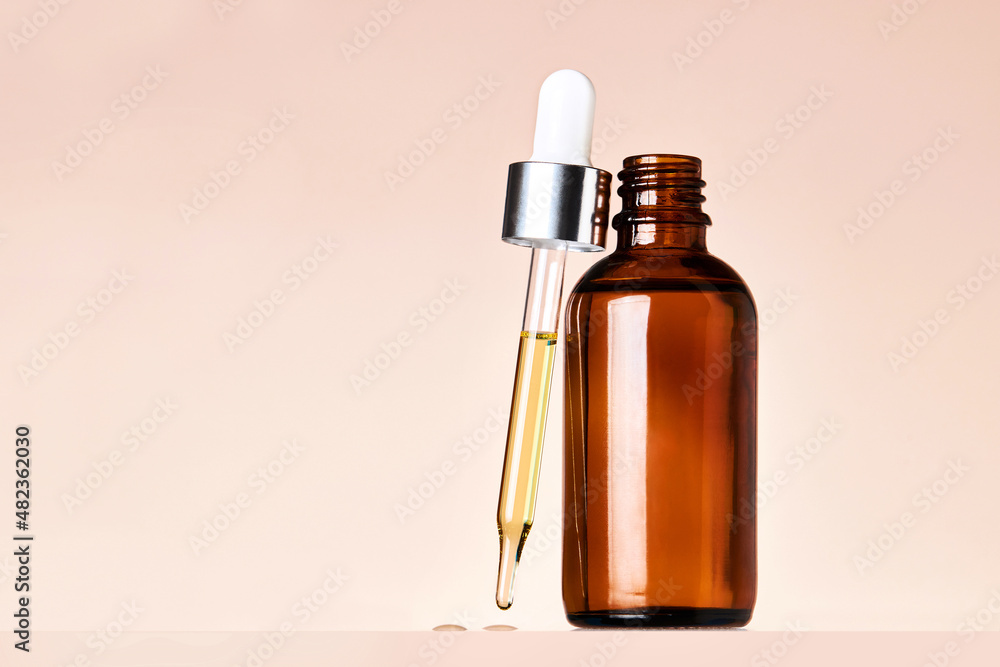 Dark glass bottle with essential oil. Dripping essential oil or serum from pipette on a beige background with copy space. Beauty care or medicine concept. Dark glass bottle with essential oil. Dripping essential oil or serum from pipette on a beige background with copy space. Beauty care or medicine concept.