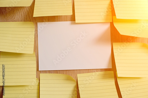 White blank piece of paper on a wooden texture background surrounded with yellow blank notes.