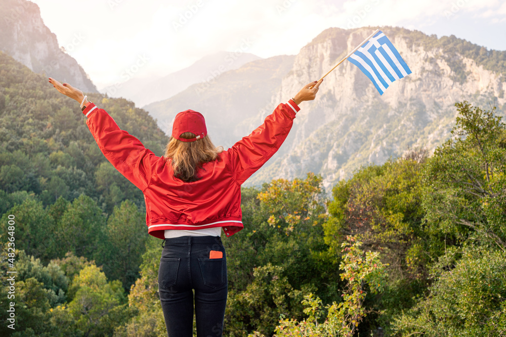A happy female tourist with a Greek flag in her hands walks along the path to the top of the famous mythological Mount Olympus. Natural parks and attractions of Greece