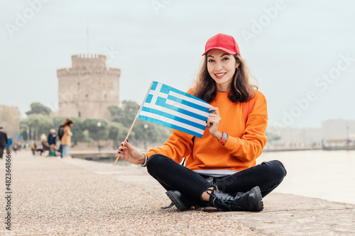 A student or immigrant girl with a Greek flag on the background of a White Tower in Thessaloniki. The concept of citizenship or learning Greek in university