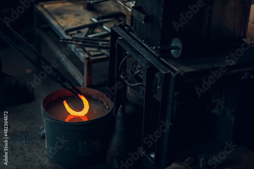 Foto Blacksmith forges and tempering metal horseshoe in jar with water at forge