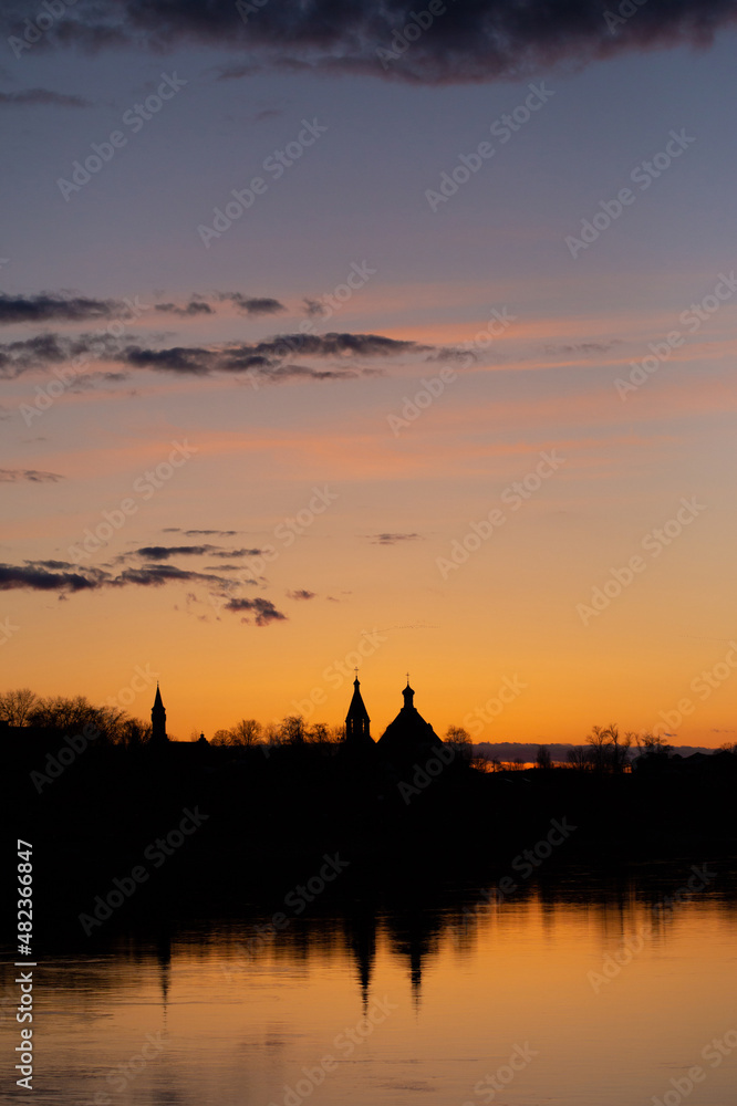 Sunset on Dnieper river. Beautiful Orange cloudy sky, city and church silhouettes reflecting in the river. Pleasant spring photo taken in Rechytsa, Belarus