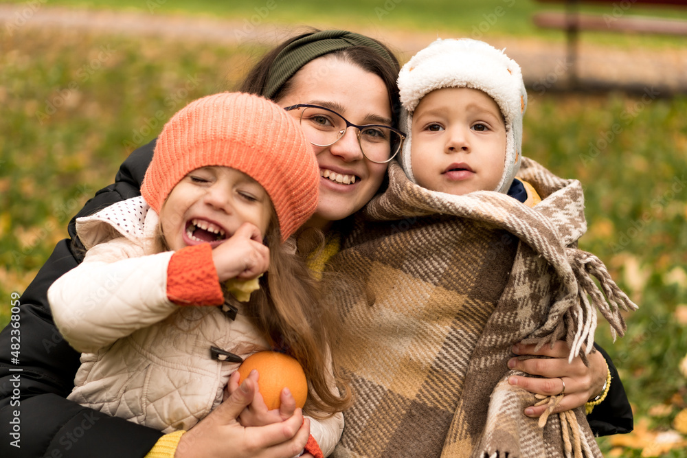 Obraz premium Young Woman Mom And Little Cute Preschool Minor Children In Orange Plaid At Yellow Fallen Leaves Nice Smiling Look At Camera In Cold Weather In Fall Park. Childhood, Family, Motherhood, Autumn Concept