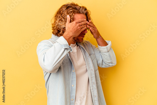 Young caucasian man isolated on yellow background afraid covering eyes with hands.