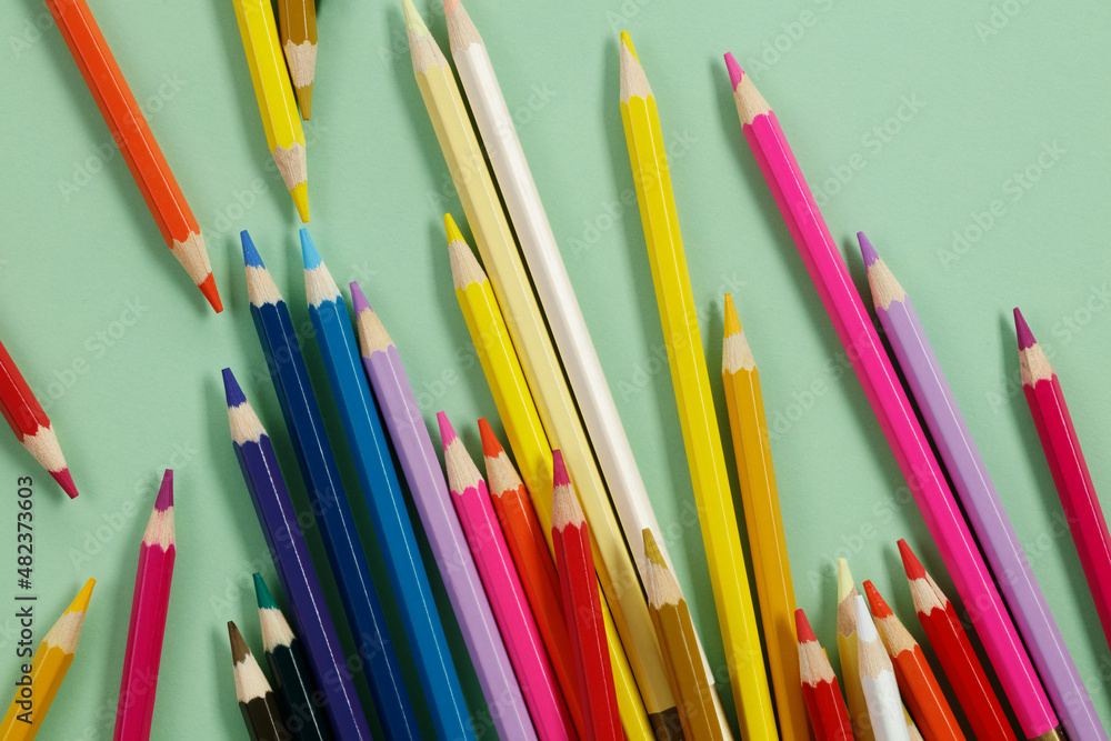 Multicolored pencils on green paper, flat lay. Drawing materials. Multicolored pencils on green paper, flat lay. Drawing materials.