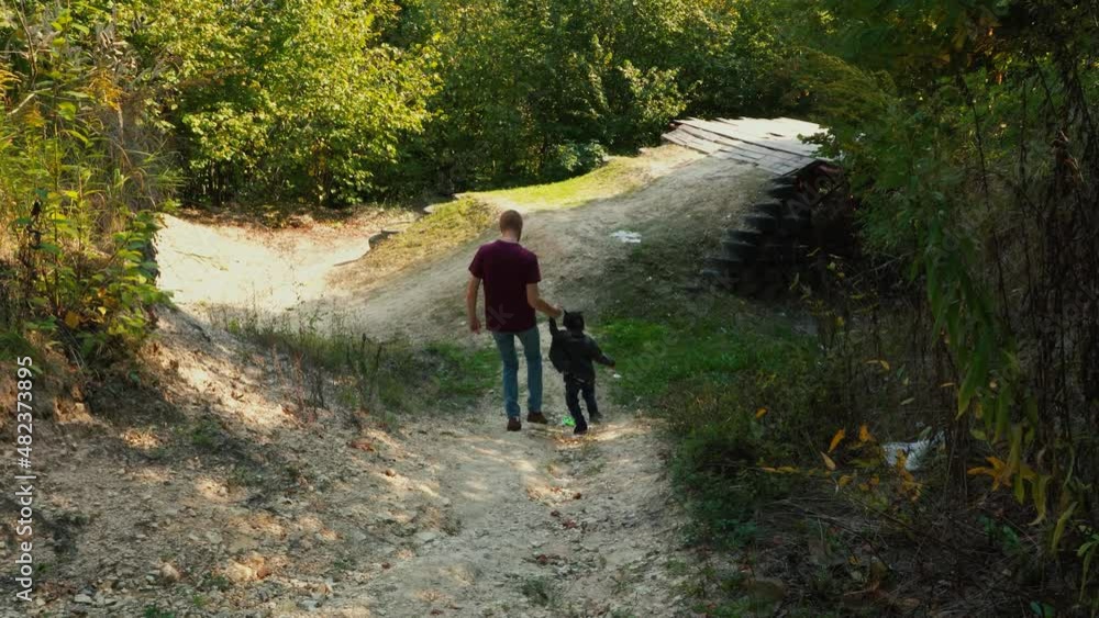 Dad and his son going down the mountain in forest, holding hands. Dad and his son going down the mountain in forest, holding hands.