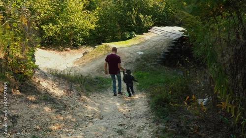 Dad and his son going down the mountain in forest, holding hands.