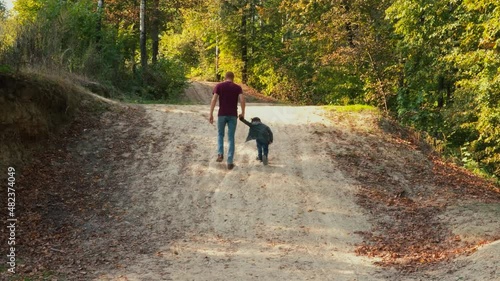 Dad and his son climbing up the mountain the mountain in forest, holding hands.