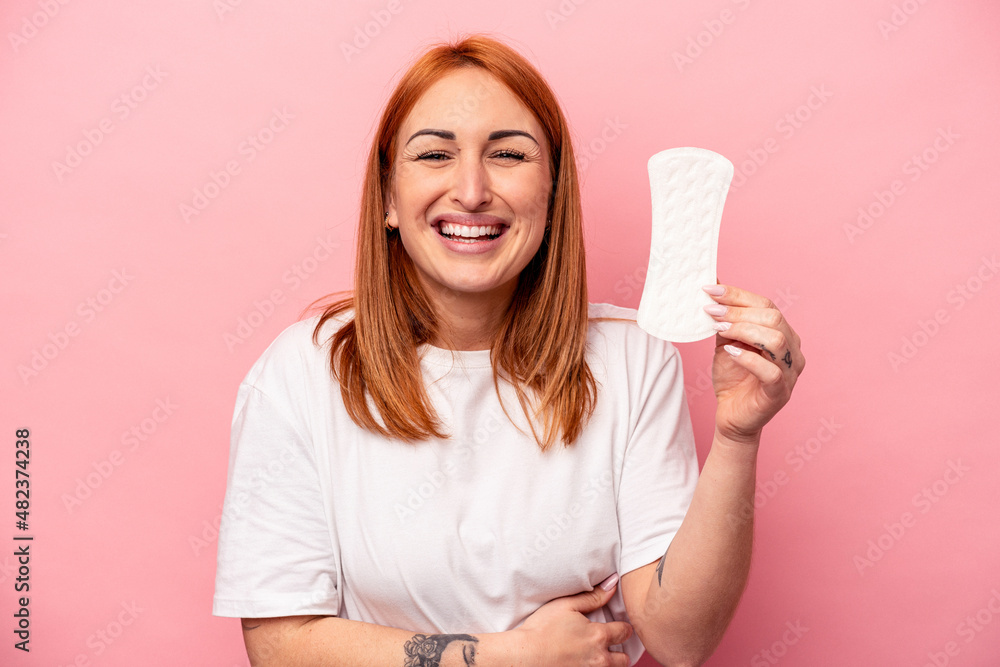 Young caucasian woman holding sanitary napkin isolated on pink background laughing and having fun. Young caucasian woman holding sanitary napkin isolated on pink background laughing and having fun.