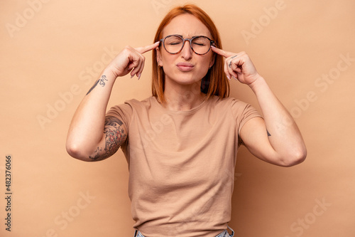 Young caucasian woman isolated on beige background focused on a task, keeping forefingers pointing head.