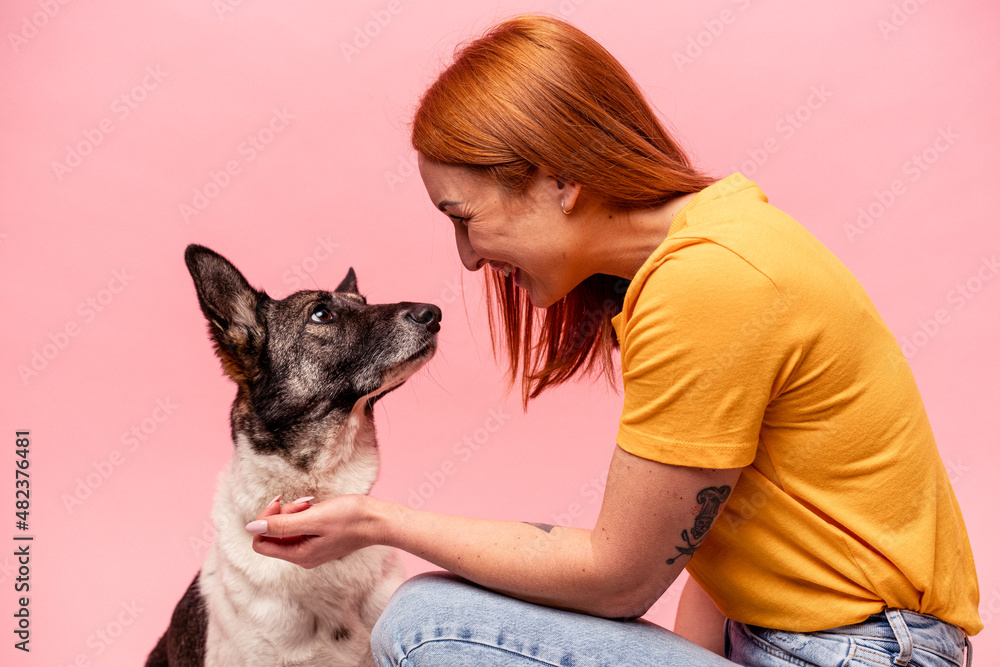 Young caucasian woman with his dog isolated on pink background