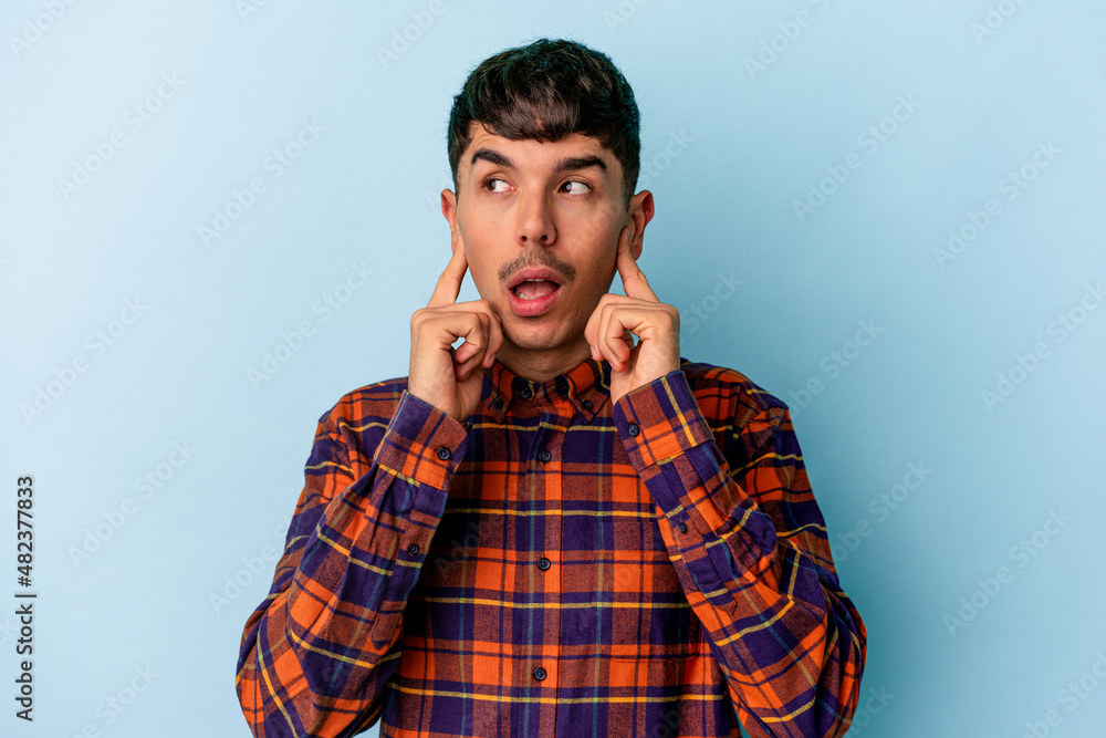 Young mixed race man isolated on blue background covering ears with fingers, stressed and desperate by a loudly ambient. Young mixed race man isolated on blue background covering ears with fingers, stressed and desperate by a loudly ambient.