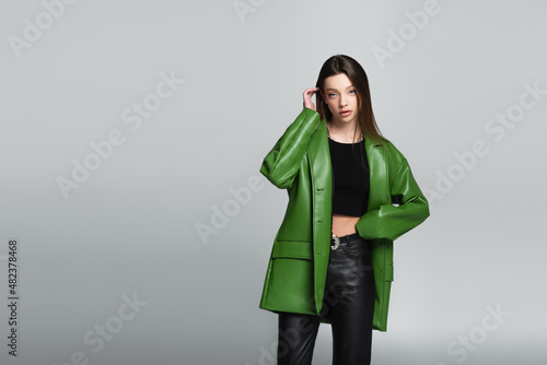 pretty woman in green jacket and black trousers standing with hand on waist isolated on grey.
