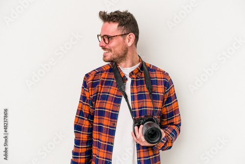 Young caucasian photograph man isolated on white background looks aside smiling, cheerful and pleasant.