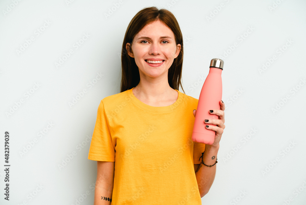 Young English woman holding a thermo isolated on blue background happy, smiling and cheerful. Young English woman holding a thermo isolated on blue background happy, smiling and cheerful.