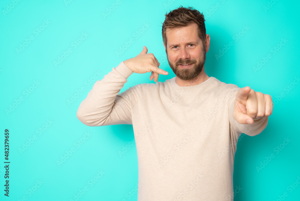 Young bearded man making call me gesture standing isolated over green background. Young bearded man making call me gesture standing isolated over green background.