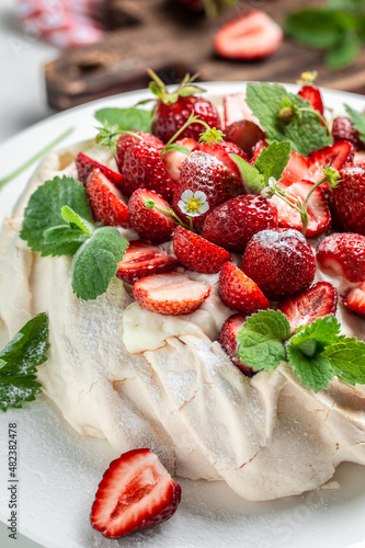 delicious homemade Pavlova cake with fresh strawberries and whipped cream. Female baker decorating delicious meringue cake  vertical image. top view. place for text