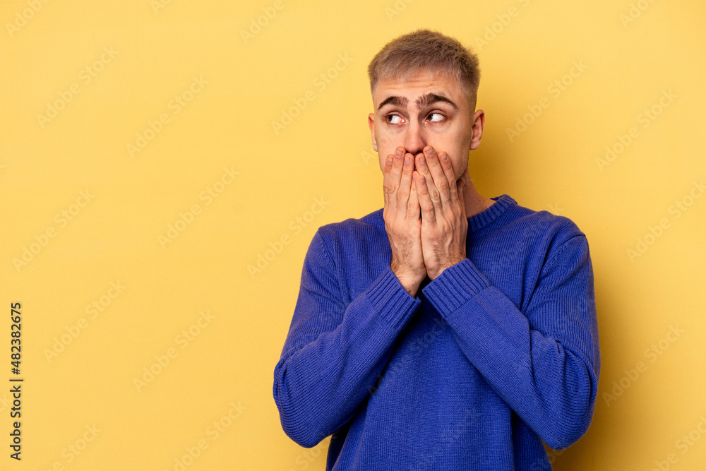 Young caucasian man isolated on yellow background thoughtful looking to a copy space covering mouth with hand.