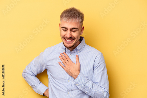 Young caucasian man isolated on yellow background laughing keeping hands on heart  concept of happiness.