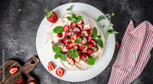 delicious homemade Pavlova cake with fresh strawberries and whipped cream. Female baker decorating delicious meringue cake, top view. place for text
