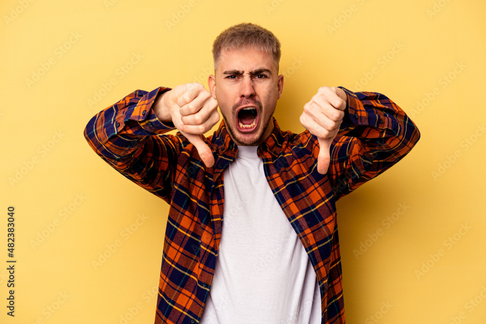 Young caucasian man isolated on yellow background showing thumb down and expressing dislike. Young caucasian man isolated on yellow background showing thumb down and expressing dislike.