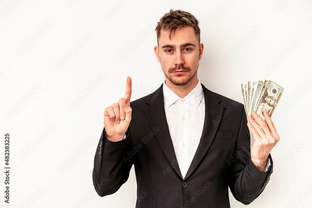Young caucasian business man holding bank notes isolated on white background showing number one with finger. Young caucasian business man holding bank notes isolated on white background showing number one with finger.