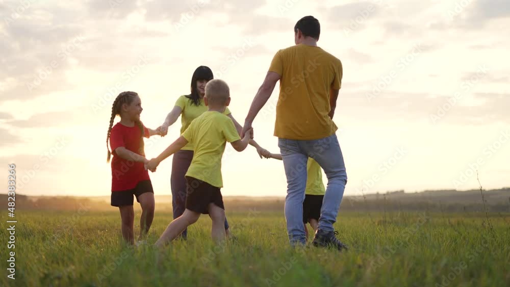 Happy family concept. Group of people hold hands in round dance. Children and parents are play in park on grass. Active lifestyle concept Family on green grass. Happy children play round dance in park Happy family concept. Group of people hold hands in round dance. Children and parents are play in park on grass. Active lifestyle concept Family on green grass. Happy children play round dance in park