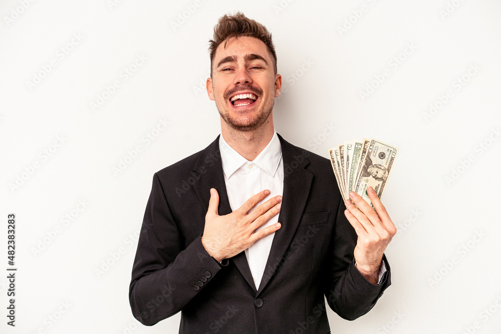 Young caucasian business man holding bank notes isolated on white background laughs out loudly keeping hand on chest. Young caucasian business man holding bank notes isolated on white background laughs out loudly keeping hand on chest.