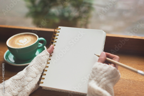 Unidentified woman is writing in the notepad in cafe.Unidentified woman is writing in the notepad in cafe. Working on bullet journal, diary, morning pages, plans and goals. Copy space for your text.