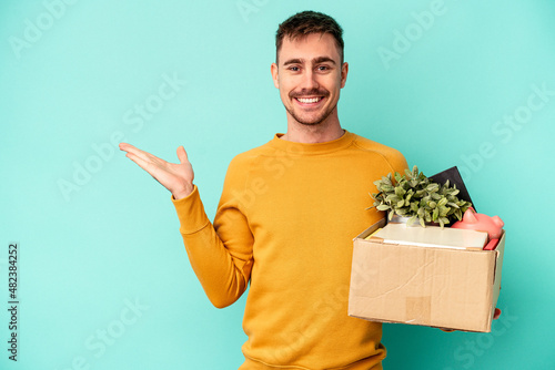 Young caucasian man making a move isolated on blue background showing a copy space on a palm and holding another hand on waist.