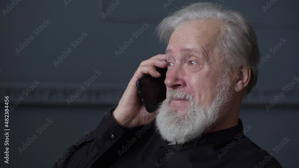Close-up face of happy bearded mature adult man with tears in eyes talking on mobile phone with family. Portrait of smiling senior aged male having pleasant conversation with grown up grandchild. Close-up face of happy bearded mature adult man with tears in eyes talking on mobile phone with family. Portrait of smiling senior aged male having pleasant conversation with grown up grandchild.