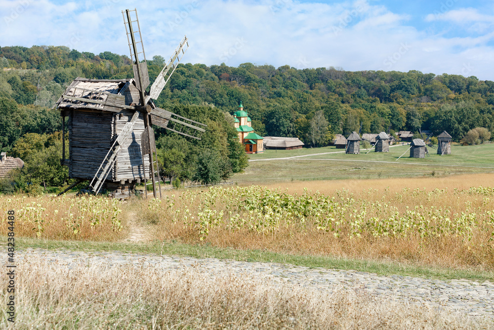 Fototapeta premium An old rural landscape with windmills against the backdrop of a lawn and dense forest.