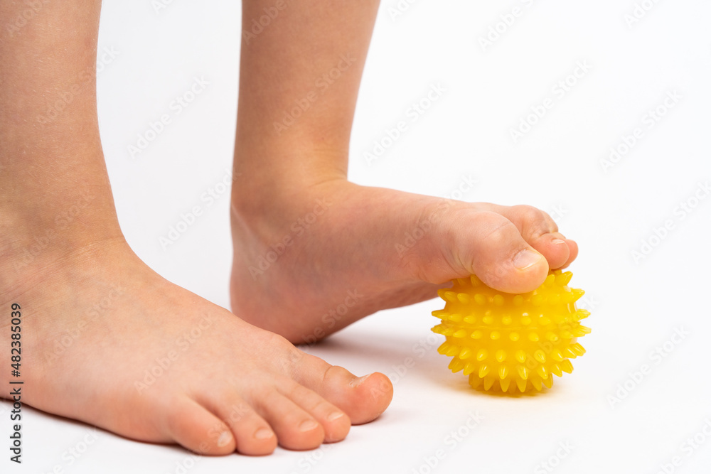 Obraz premium yellow needle ball for massage and physical therapy on a white background with a child's foot, the concept of prevention and treatment of foot valgus