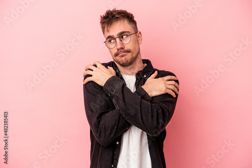 Young caucasian man isolated on pink background hugs, smiling carefree and happy.