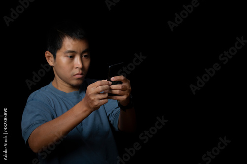 Portrait of a young man using smartphone on black background.