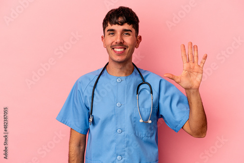 Young mixed race nurse man isolated on pink background smiling cheerful showing number five with fingers. © Asier