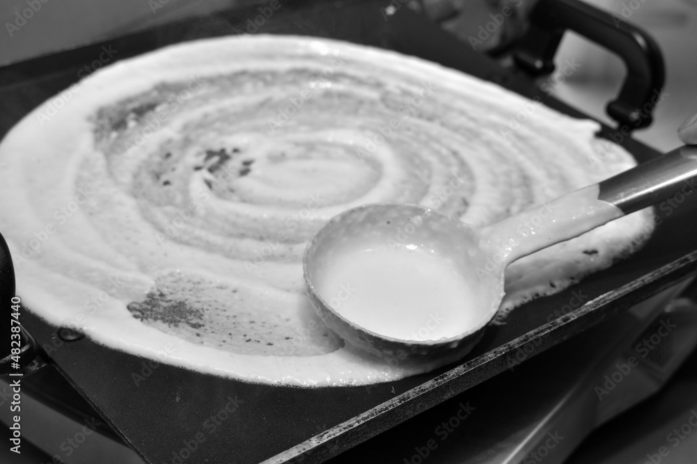 Cooking round south indian dish(dosa) with white batter and ladle on hot non stick pan with hot vapour coming out Cooking round south indian dish(dosa) with white batter and ladle on hot non stick pan with hot vapour coming out