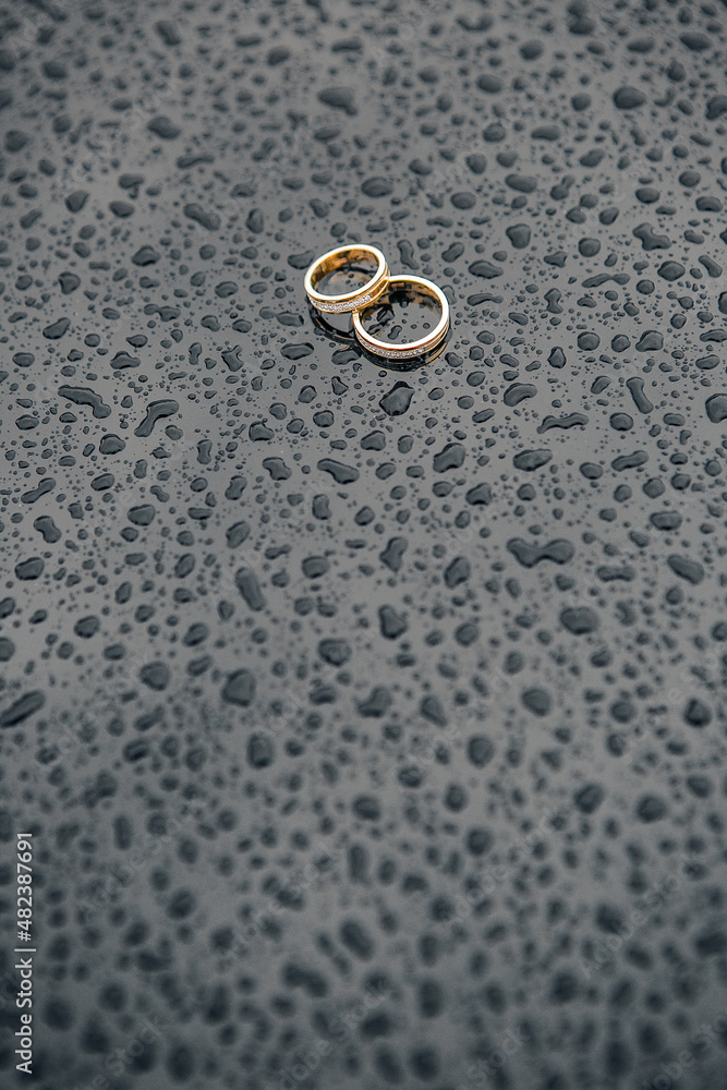 two gold wedding rings against a background of glossy black metal covered with raindrops two gold wedding rings against a background of glossy black metal covered with raindrops
