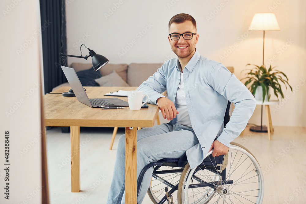 Cheerful disabled man in wheelchair is at home Cheerful disabled man in wheelchair is at home