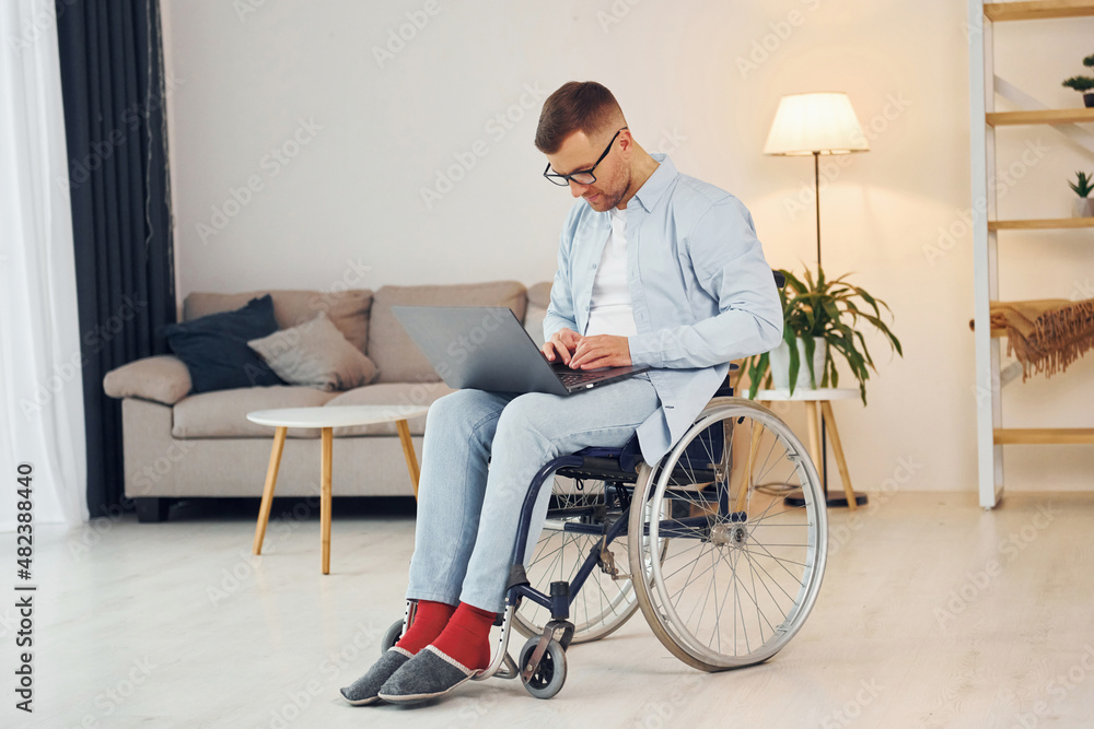 With laptop on the legs. Disabled man in wheelchair is at home With laptop on the legs. Disabled man in wheelchair is at home