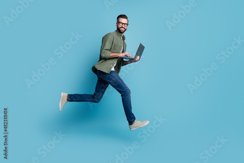 Profile photo of sporty active guy jump hold netbook run work wear specs green shirt isolated blue color background
