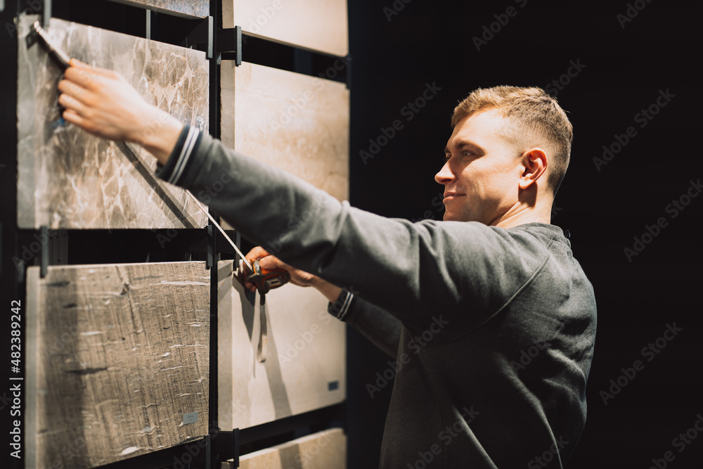 Male designer using a tape measure to measure granite samples in a specialized store selling natural stone and granite, house renovation Male designer using a tape measure to measure granite samples in a specialized store selling natural stone and granite, house renovation