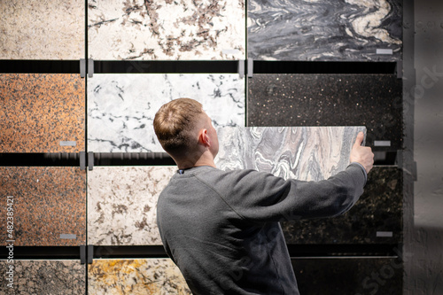 a man in a hypermarket next to a rack with natural, ceramic tiles for ll and floor decoration, home renovation and construction concept