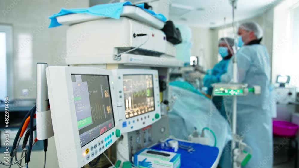 Innovative equipment working during operation. Two screens showing patient’s vital signs at surgery. Doctors operating at the backdrop in blur. Innovative equipment working during operation. Two screens showing patient’s vital signs at surgery. Doctors operating at the backdrop in blur.