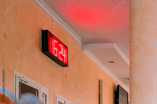 A red digital board on the wall shows time 16:24. Date. Red led electronic scoreboard indoor. Railway station. Public space. European