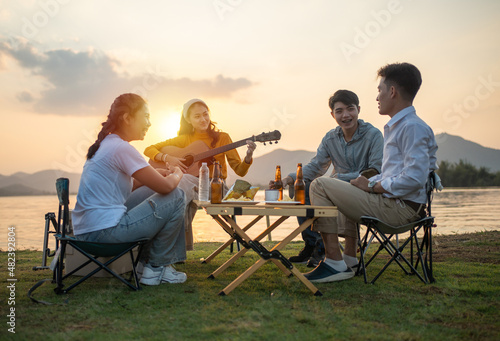 happy group of Asian friends Play guitar and sing enjoying camping and drinking beer