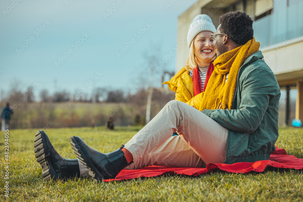 Young beautiful couple blonde girl in warm clothes and man in white t-shirt having fun in the grass in a field in nature at sunset. Happy young loving couple sitting, laughing and hugging Young beautiful couple blonde girl in warm clothes and man in white t-shirt having fun in the grass in a field in nature at sunset. Happy young loving couple sitting, laughing and hugging